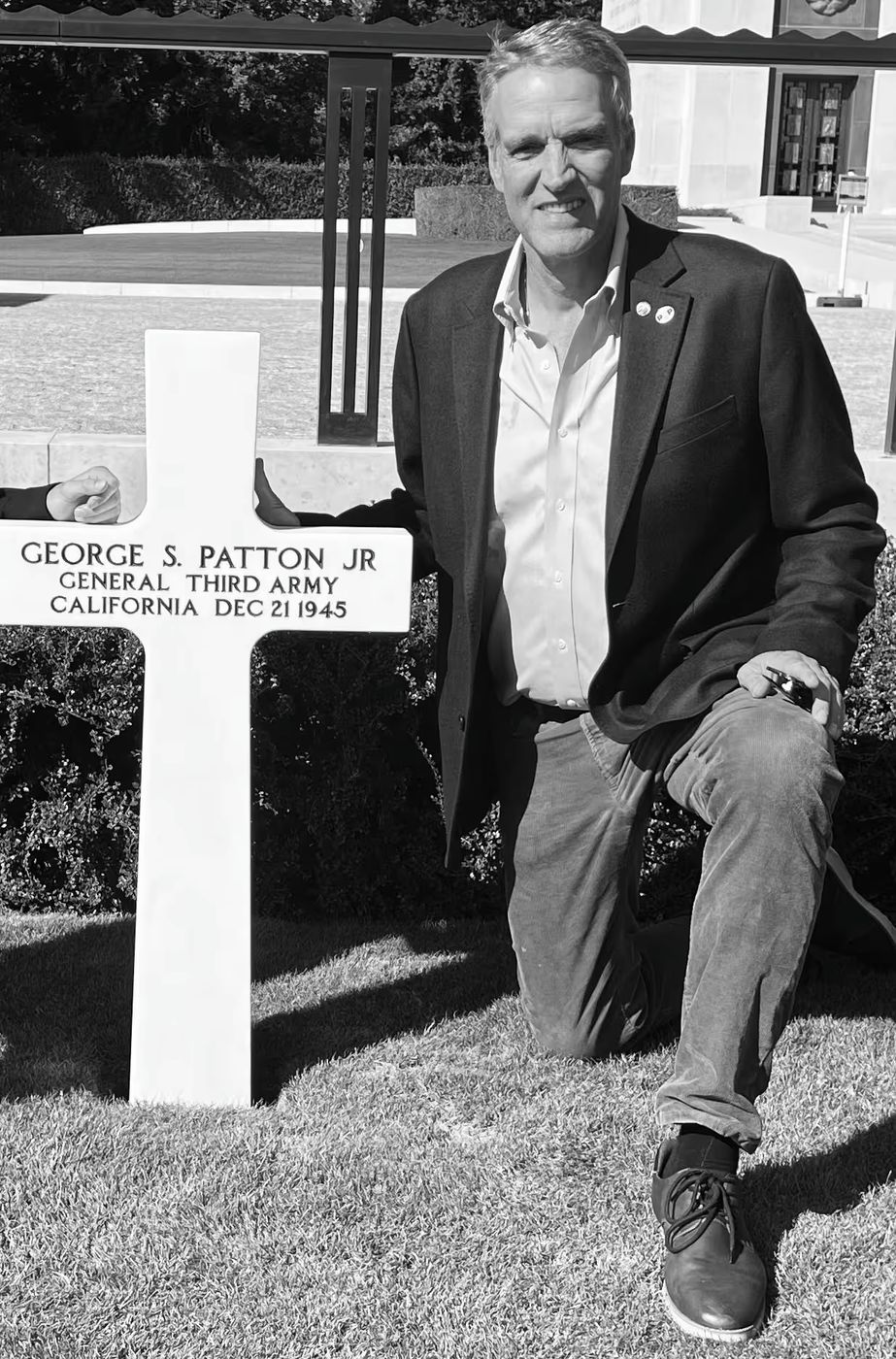 Benjamin Patton kneeling beside the white cross of General George S. Patton Jr.
