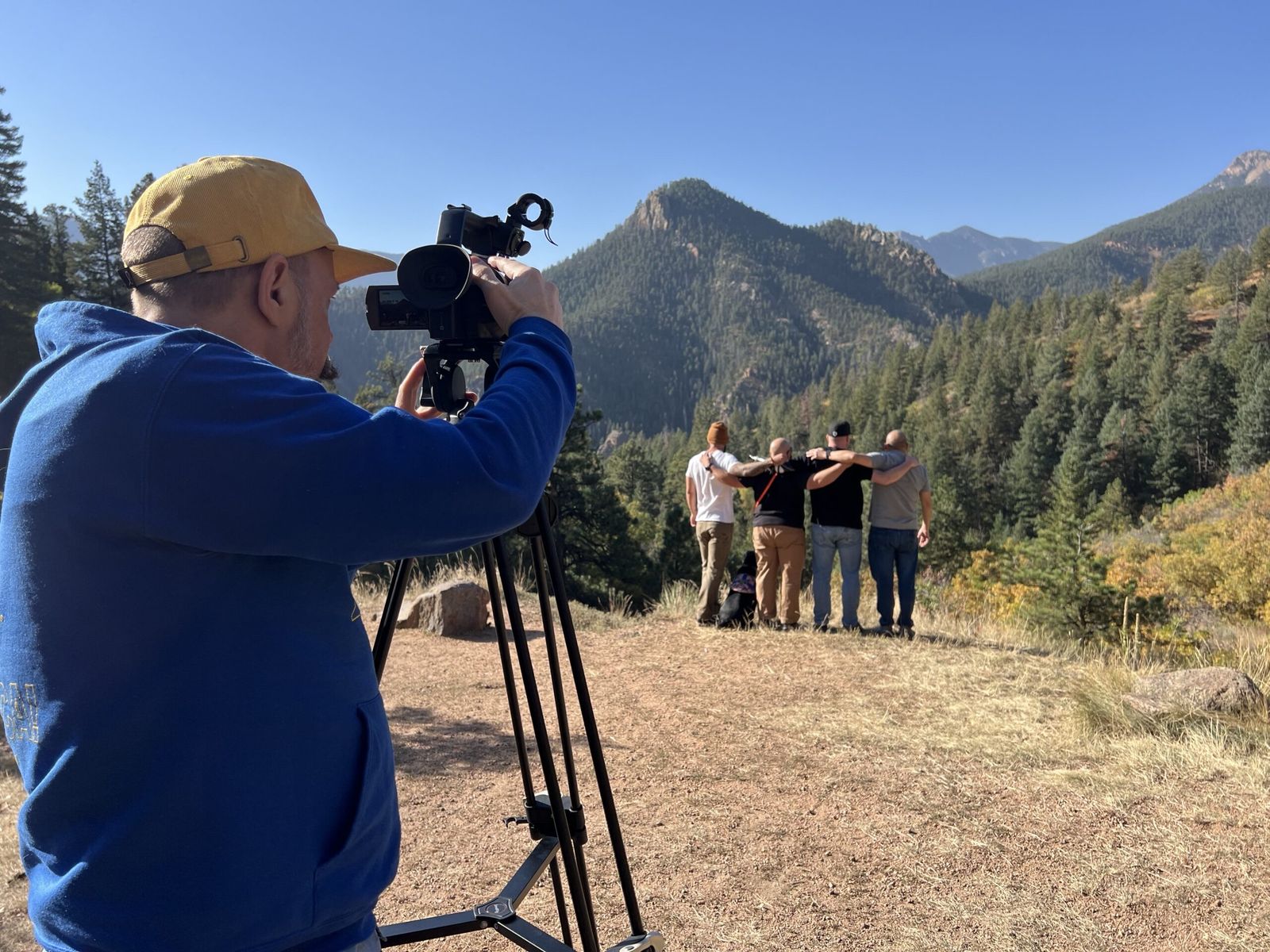 Ben behind a film camera on a mountainside, filming a group of veterans standing arm in arm